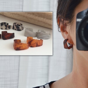 Könnte beinhalten: Ein Set mit sechs Resin-Creolen in drei verschiedenen Farben und Mustern: Braun mit Marmorierung, Grau mit Marmorierung und schwarz-weißem Tiermuster. Die Ohrringe sind auf einer weißen Oberfläche und am Ohr einer Person zu sehen.