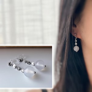 Elegante Ohrclips mit runden weißen Achatperlen und floraler Silberkette. Ideal für einen raffinierten und zeitlosen Touch.