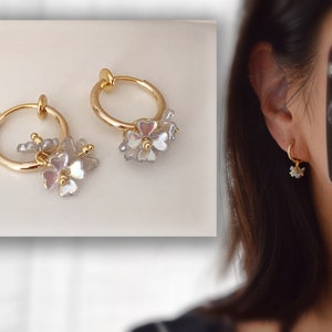 Op de afbeelding: Gouden creolen met een cluster van witte en roze bloemencharms die aan elke creool hangen.