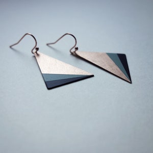 May include: A pair of triangle-shaped earrings with a geometric design. The earrings are made of metal and have a gold, green, and black color scheme.
