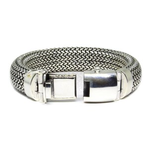 May include: A silver bracelet with a woven chain design and a silver clasp.