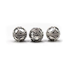 May include: Three silver-colored, spherical beads with intricate designs. Each bead features a pattern of oval shapes and small dots, with a rope-like texture around the center. The beads are displayed against a white background.