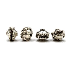 May include: Four silver beads with a textured design. Each bead has a small hole in the center for stringing.