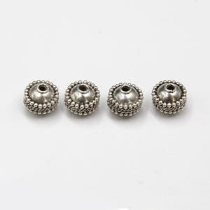 May include: Four silver-toned round beads with a textured surface and a hole in the center.