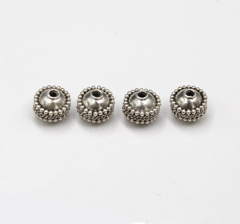 May include: Four silver-toned round beads with a textured surface and a hole in the center.