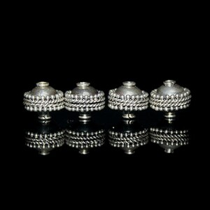 May include: Four silver metal beads with a decorative beaded design. The beads are arranged in a row on a black background.