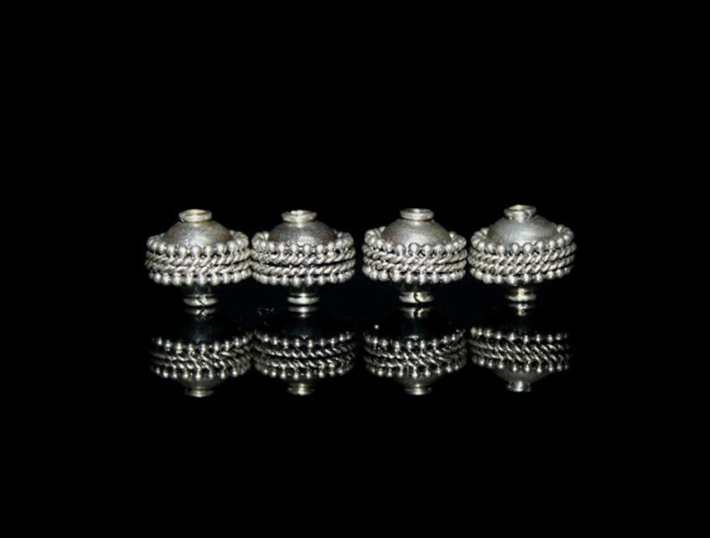 May include: Four silver metal beads with a decorative beaded design. The beads are arranged in a row on a black background.