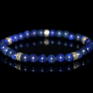 May include: A blue lapis lazuli beaded bracelet with silver accents. The bracelet is made of round beads and is strung on a stretchy cord.