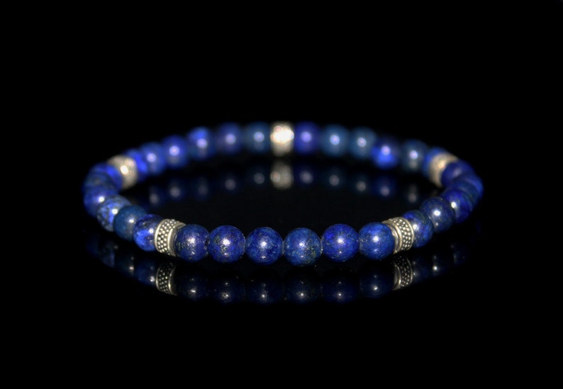 May include: A blue lapis lazuli beaded bracelet with silver accents. The bracelet is made of round beads and is strung on a stretchy cord.