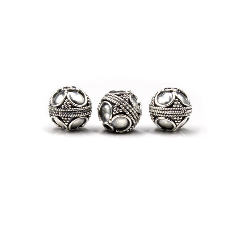 May include: Three silver-colored, spherical beads. Each bead features a pattern of raised, oval shapes and small dots, with a band of twisted metal around the center. The beads are displayed against a white background.