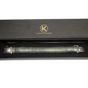May include: A silver bracelet with a textured design, in a black box with the text "Kartini Studio" and a gold "K" logo.