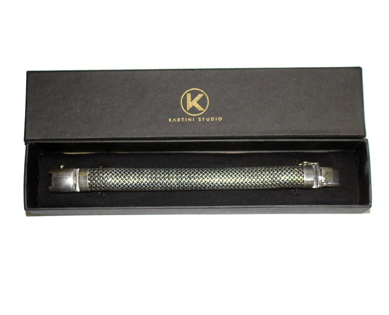 May include: A silver bracelet with a textured design, in a black box with the text "Kartini Studio" and a gold "K" logo.