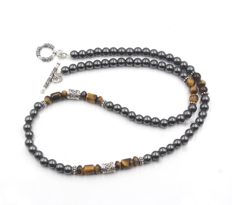 Puede incluir: Un collar de cuentas de hematites negro y ojo de tigre con un cierre de palanca de plata. El collar presenta cuentas alternas de hematites negro y ojo de tigre.