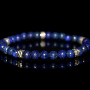 May include: A blue lapis lazuli beaded bracelet with silver accents. The bracelet is made of round beads and has a simple design.