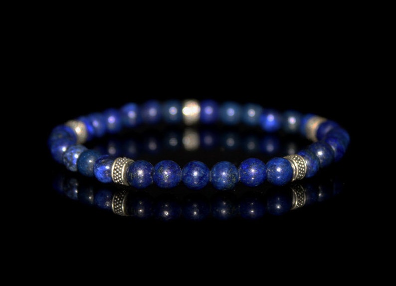 May include: A blue lapis lazuli beaded bracelet with silver accents. The bracelet is made of round beads and has a simple design.