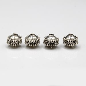 May include: Four silver bead caps with a textured design. The bead caps are round and have a hole in the center.