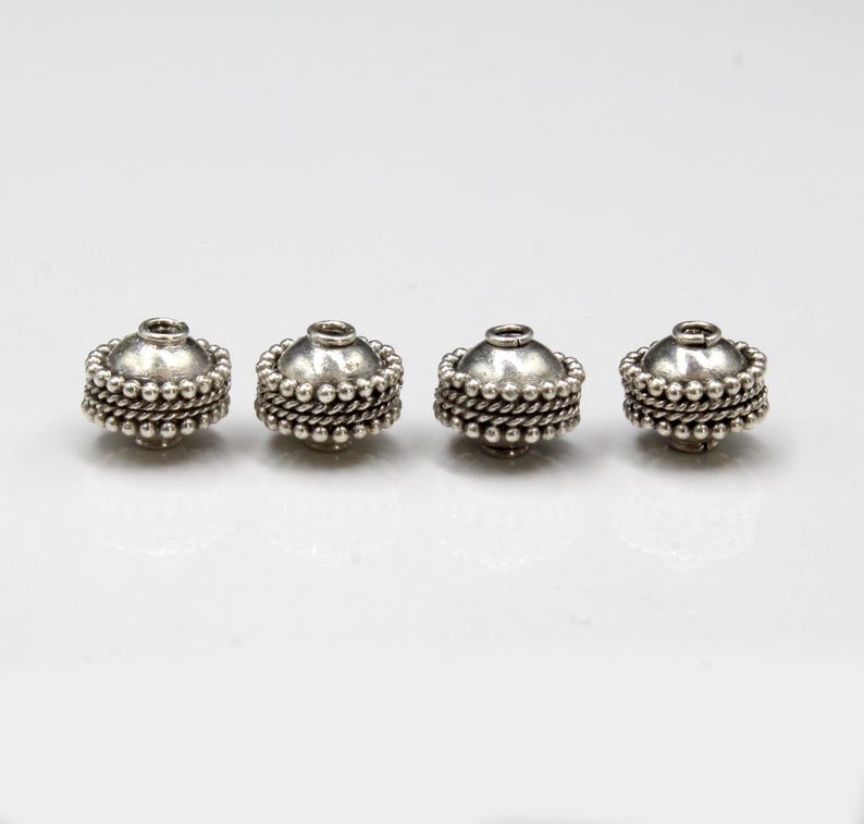 May include: Four silver bead caps with a textured design. The bead caps are round and have a hole in the center.
