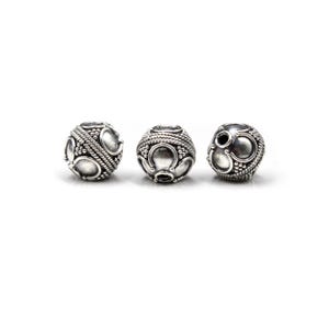 May include: Three silver-colored, spherical beads with intricate designs. Each bead features a pattern of raised dots, curved shapes, and braided rope-like details. The beads are displayed against a plain white background.