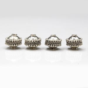 May include: Four silver beads with a beaded design around the center. The beads have a hole in the center for stringing.