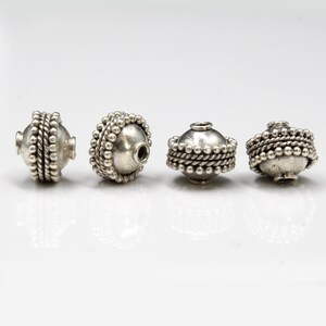 May include: Four silver beads with a textured, beaded design. The beads are round and have a hole in the center for stringing.