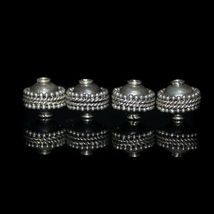 May include: Four silver-toned metal beads with a decorative beaded trim. The beads are round and have a domed top.