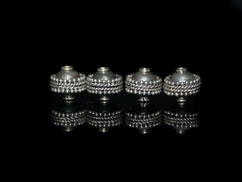 May include: Four silver-toned metal beads with a decorative beaded trim. The beads are round and have a domed top.