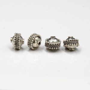 May include: Four silver beads with a textured, beaded design. The beads are round and have a hole in the center.