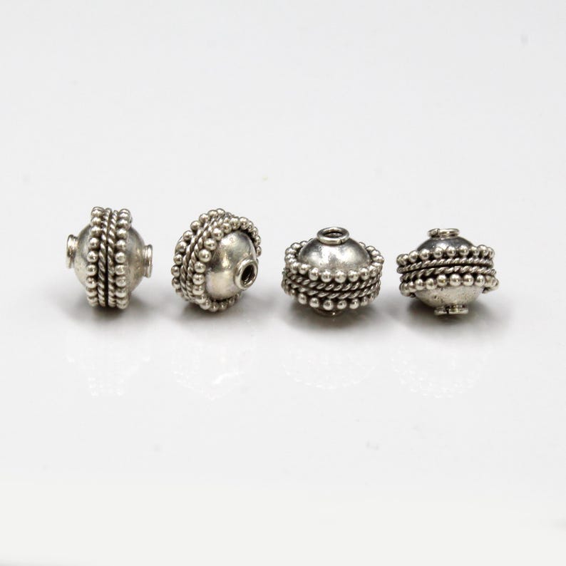 May include: Four silver beads with a textured, beaded design. The beads are round and have a hole in the center.