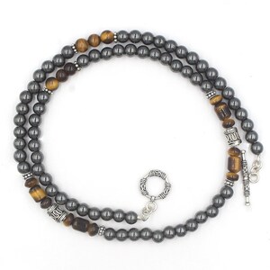 Puede incluir: Un collar de doble cadena con cuentas de hematites grises y cuentas de ojo de tigre. El collar tiene detalles plateados y un cierre plateado.