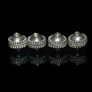 May include: Four silver-toned metal beads with a beaded edge. The beads are round and have a smooth, shiny finish.