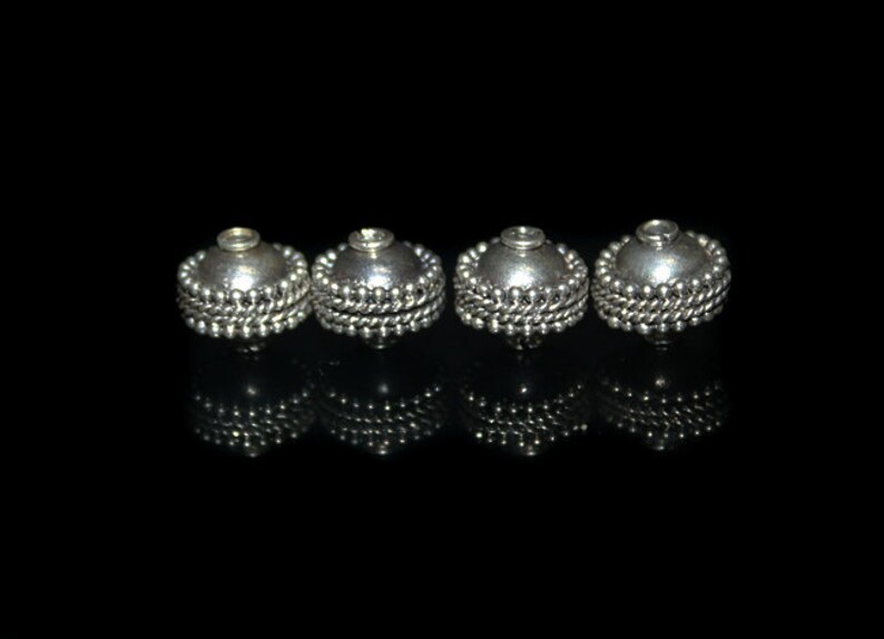 May include: Four silver-toned metal beads with a beaded edge. The beads are round and have a smooth, shiny finish.