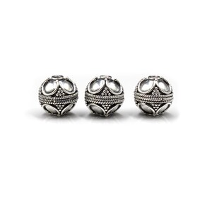 May include: Three silver-colored, spherical beads. Each bead features a decorative pattern of curved shapes and a rope-like band around the center. The beads are displayed against a white background, highlighting their intricate design.
