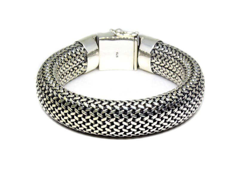 May include: A silver bracelet with a woven chain design. The bracelet is made of a thick, braided chain that is smooth and shiny.