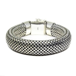 May include: A silver bracelet with a woven chain design. The bracelet has a clasp closure and is marked "925" on the clasp.