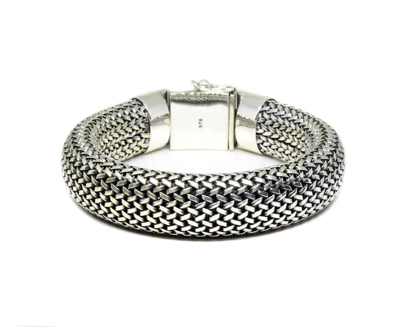 May include: A silver bracelet with a woven chain design. The bracelet has a clasp closure and is marked "925" on the clasp.