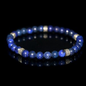 May include: A blue gemstone bracelet with silver accents. The bracelet is made of round beads and is strung on a stretchy cord.
