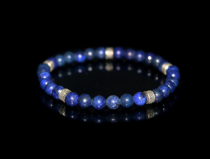 May include: A blue gemstone bracelet with silver accents. The bracelet is made of round beads and is strung on a stretchy cord.