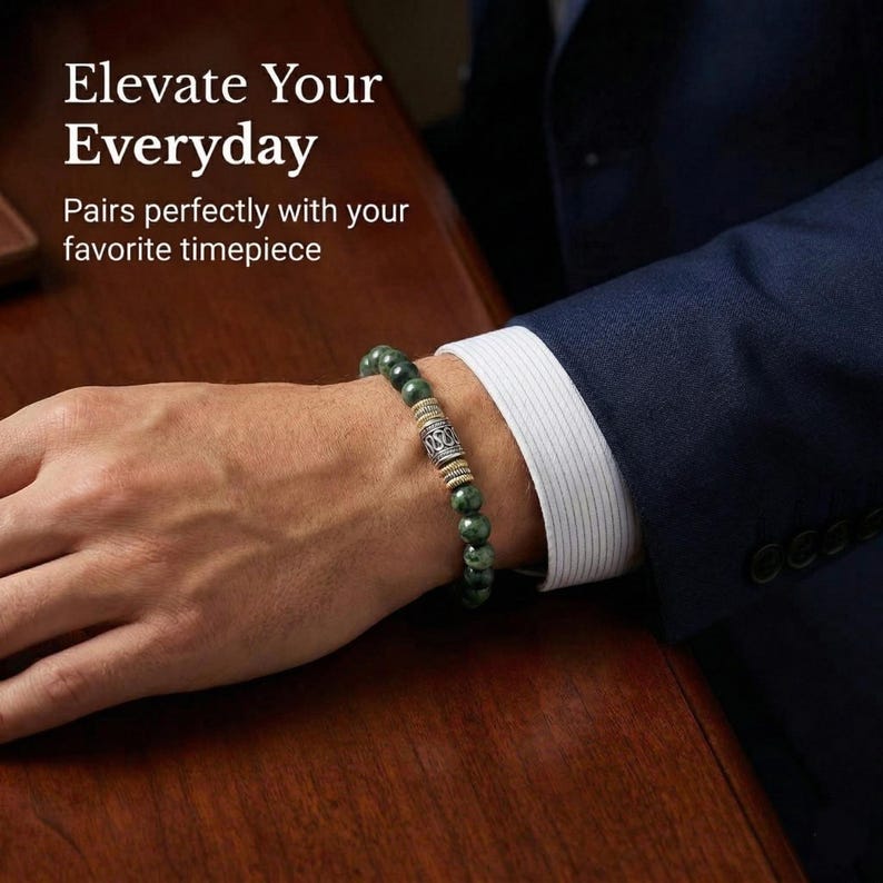 Pu&ograve; includere: Un braccialetto di perline verdi con un elemento decorativo argentato e dorato &egrave; indossato al polso. Il braccialetto &egrave; abbinato a un abito blu navy e a una camicia bianca. Il testo "Elevate Your Everyday" &egrave; visibile.
