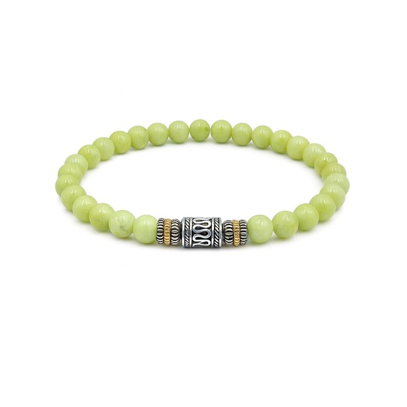 Op de afbeelding: Een armband met lichtgroene, ronde kralen. De armband heeft een zilverkleurige centrale kraal met een golvend ontwerp, geflankeerd door goudkleurige en zilverkleurige afstandskralen. De armband wordt op een witte achtergrond getoond.