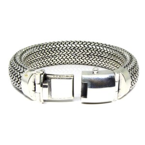 May include: A silver bracelet with a woven chain design and a clasp closure.