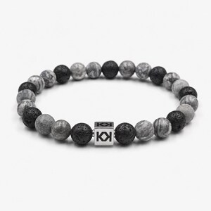 May include: A beaded bracelet featuring a mix of gray, black, and marbled stone beads. A silver cube with a logo is centered on the bracelet. The beads are round and have a natural, textured appearance.
