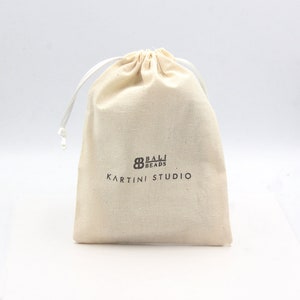 May include: A white cotton drawstring bag with the text "Bali Beads Kartini Studio" printed in brown.