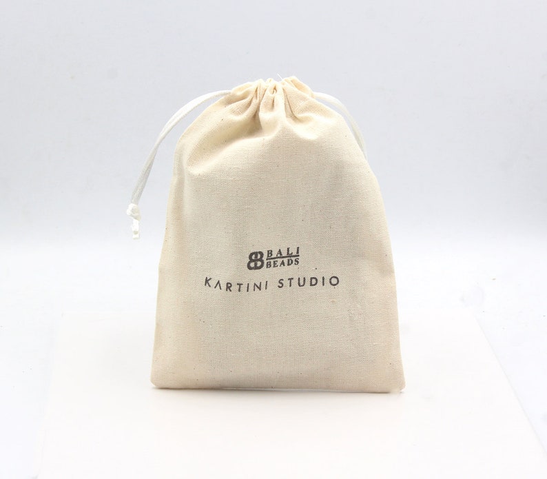 May include: A white cotton drawstring bag with the text "Bali Beads Kartini Studio" printed in brown.