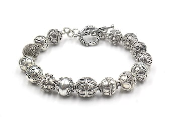 May include: A silver bracelet with a toggle clasp and multiple round beads with intricate designs.