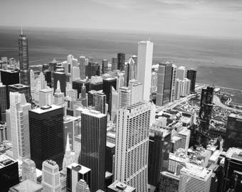 Puede incluir: Una vista aérea en blanco y negro de un horizonte urbano con muchos edificios altos. Los edificios están agrupados y algunos son más altos que otros. La ciudad está ubicada en un cuerpo de agua.