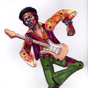 May include: A paper doll of a musician playing a guitar. The doll is wearing a purple shirt, green pants, and a brown headband. The guitar is white with black accents.