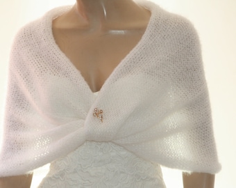 May include: White knitted shawl with a delicate openwork pattern. The shawl is draped over a mannequin's shoulders and fastened with a small gold brooch.