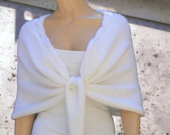 Pode incluir: Xale de malha branca com um broche de imitação de pérola, usado sobre uma blusa branca.