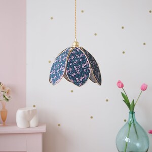 Peut inclure: Un luminaire suspendu doré avec un abat-jour à motif floral. L'abat-jour est en tissu et présente un motif floral bleu et rose. La lumière est suspendue à un plafond blanc.