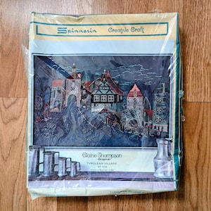 May include: A sealed craft kit featuring a cross-stitch design of a Tyrolean village. The kit includes the text "Spinnerin Creative Craft" and "Elaine Thompson Original". The finished size is 24 x 36 inches.